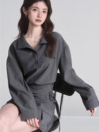 Model wearing a grey long-sleeved collared shirt and a grey asymmetrical skirt with pleats.