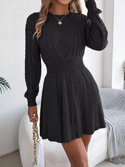 Woman wearing a black long-sleeved knit dress with cable knit detailing, holding a gold chain purse.