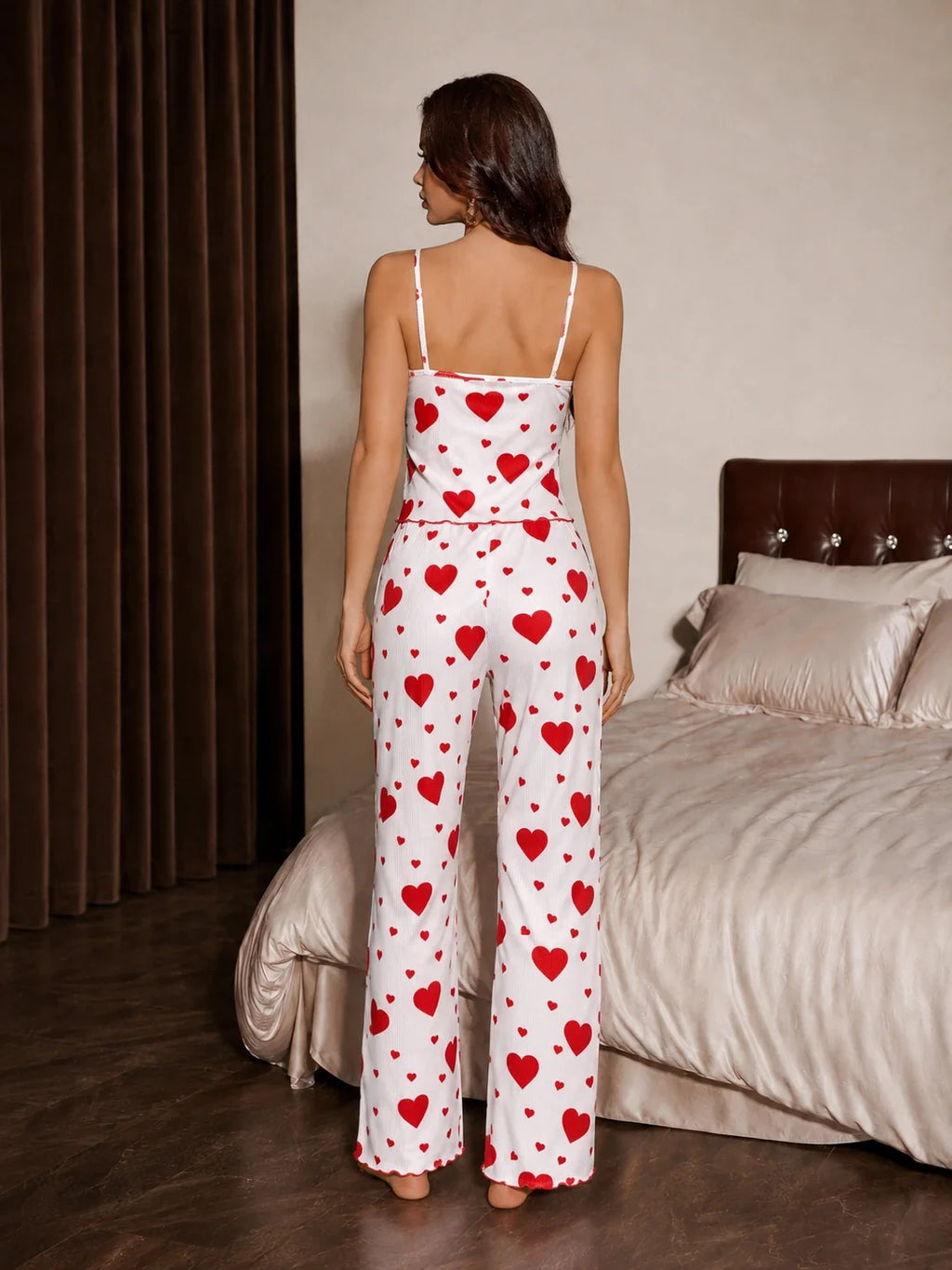 Back view of a woman wearing a white and red heart print pajama set with spaghetti straps and a drawstring waist.