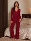 Front view of a woman wearing a red ribbed knit pajama set with lace trim, featuring a wrap top and wide leg pants, standing in a bedroom.