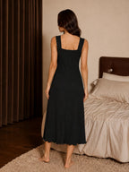 Back view of a woman wearing a black rib-knit midi nightdress with a square back, standing in a bedroom.