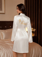 Back view of a woman wearing a white satin bridal robe with 'Bride' and a crown embroidered in gold