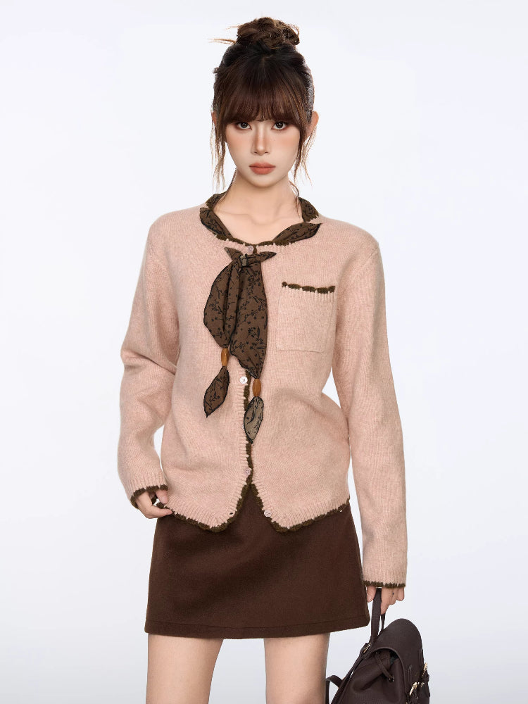 Model wearing a pink knit cardigan with brown trim and a floral scarf.