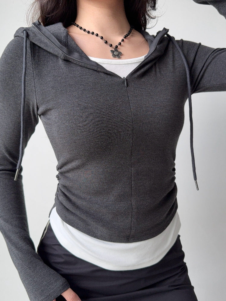 Woman adjusting her dark grey hooded zip-up top, revealing the white tank underneath.