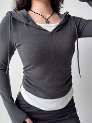 Woman adjusting her dark grey hooded zip-up top, revealing the white tank underneath.