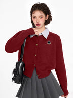 Woman wearing a burgundy knit cardigan over a striped collared shirt, paired with a grey pleated skirt and a black backpack.