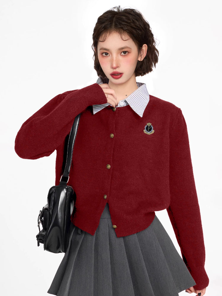 Woman wearing a burgundy knit cardigan over a striped collared shirt, paired with a grey pleated skirt and a black backpack.