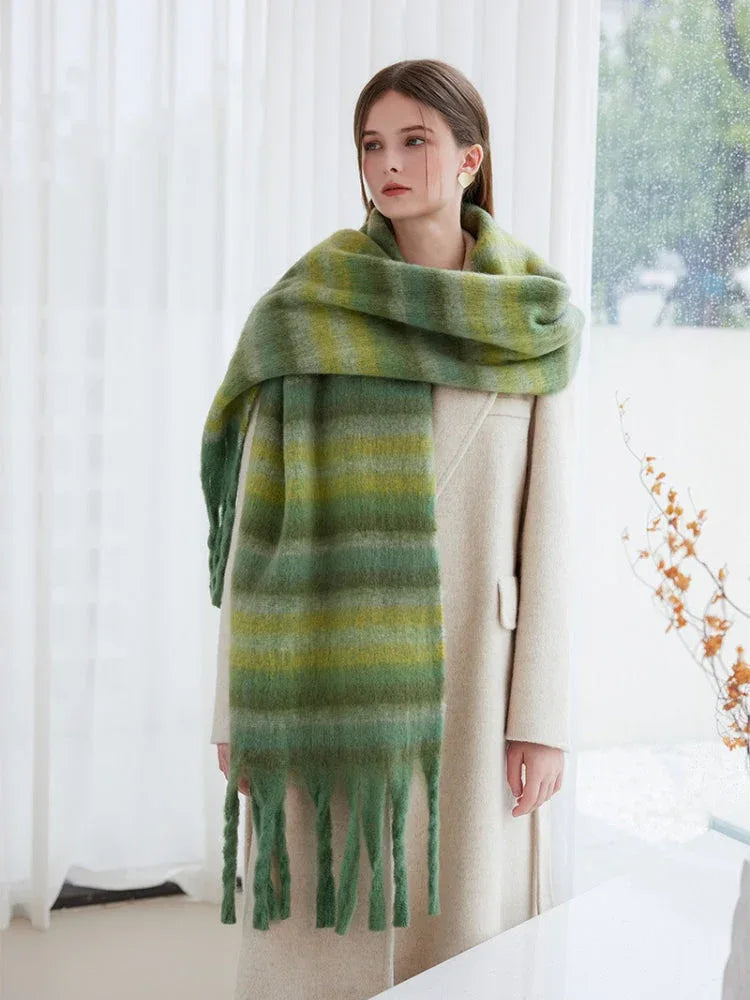 Woman wearing a cream coat and a long, oversized green striped scarf with fringe detail.