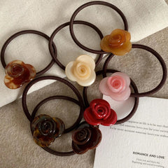 Several rose-shaped hair ties are scattered on a textured surface, with a piece of paper containing text in the background.