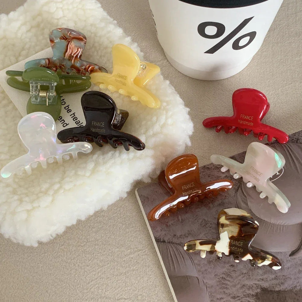 Various acetate claw hair clips arranged on a textured surface, with a coffee cup in the background