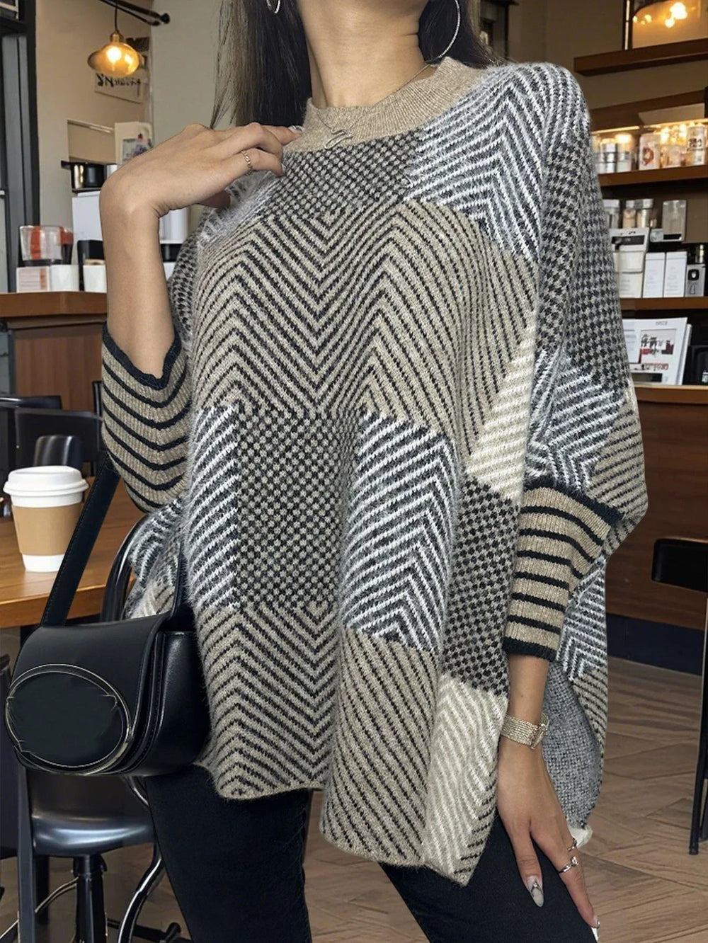 Woman wearing a geometric pattern knit poncho and black pants, holding a black handbag