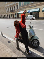 Woman wearing a red fur jacket and black pants leaning on a pole next to a scooter
