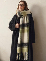 woman wearing a dark coat and a green and white plaid scarf, adjusting the scarf with her hand