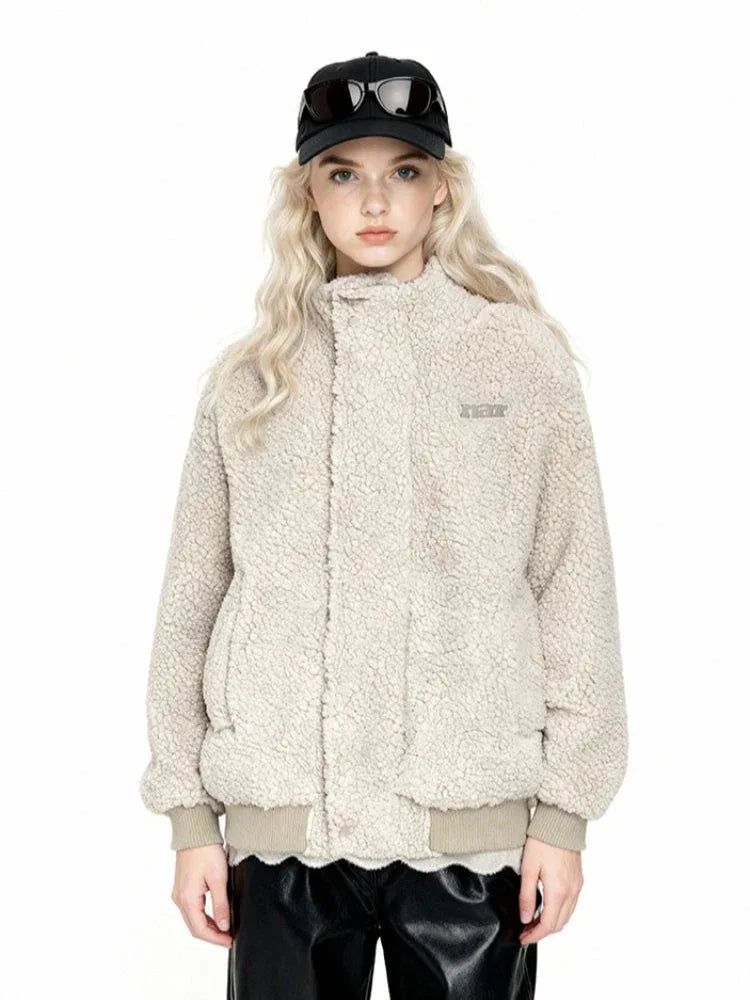 Front view of a woman wearing a cream-colored sherpa fleece bomber jacket, black faux leather pants, and a black baseball cap with sunglasses.