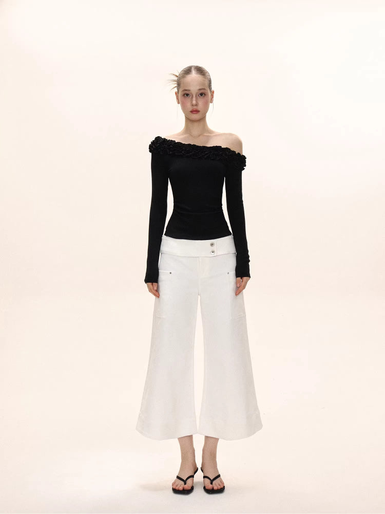 Full-body shot of a model in a black off-the-shoulder long-sleeved top with ruffles and white wide-leg cropped pants.