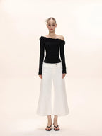Full-body shot of a model in a black off-the-shoulder long-sleeved top with ruffles and white wide-leg cropped pants.