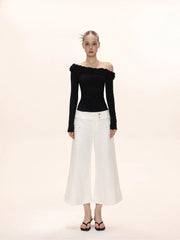Full-body shot of a model in a black off-the-shoulder long-sleeved top with ruffles and white wide-leg cropped pants.