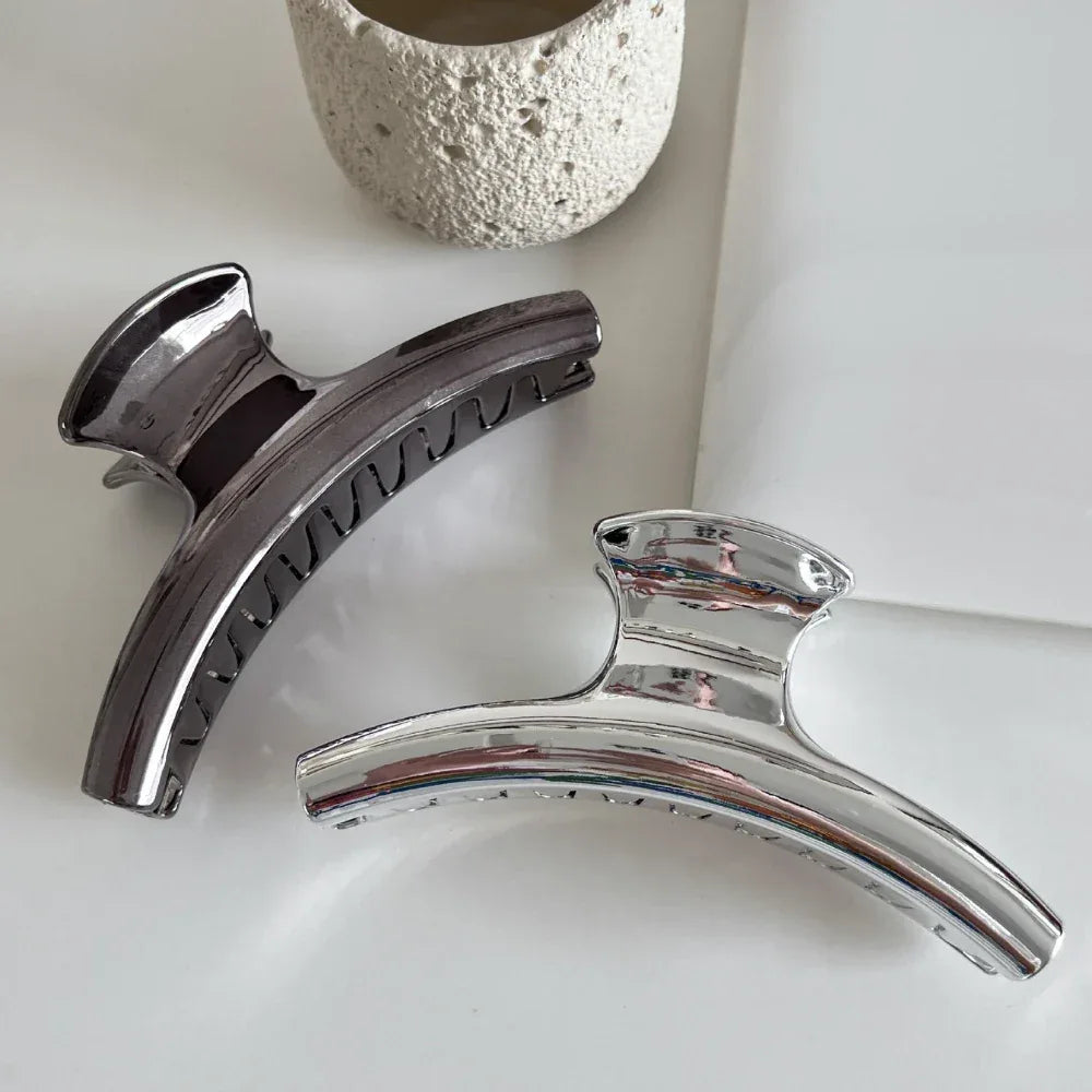 Two metallic claw clips, one silver and one dark grey, on a white surface