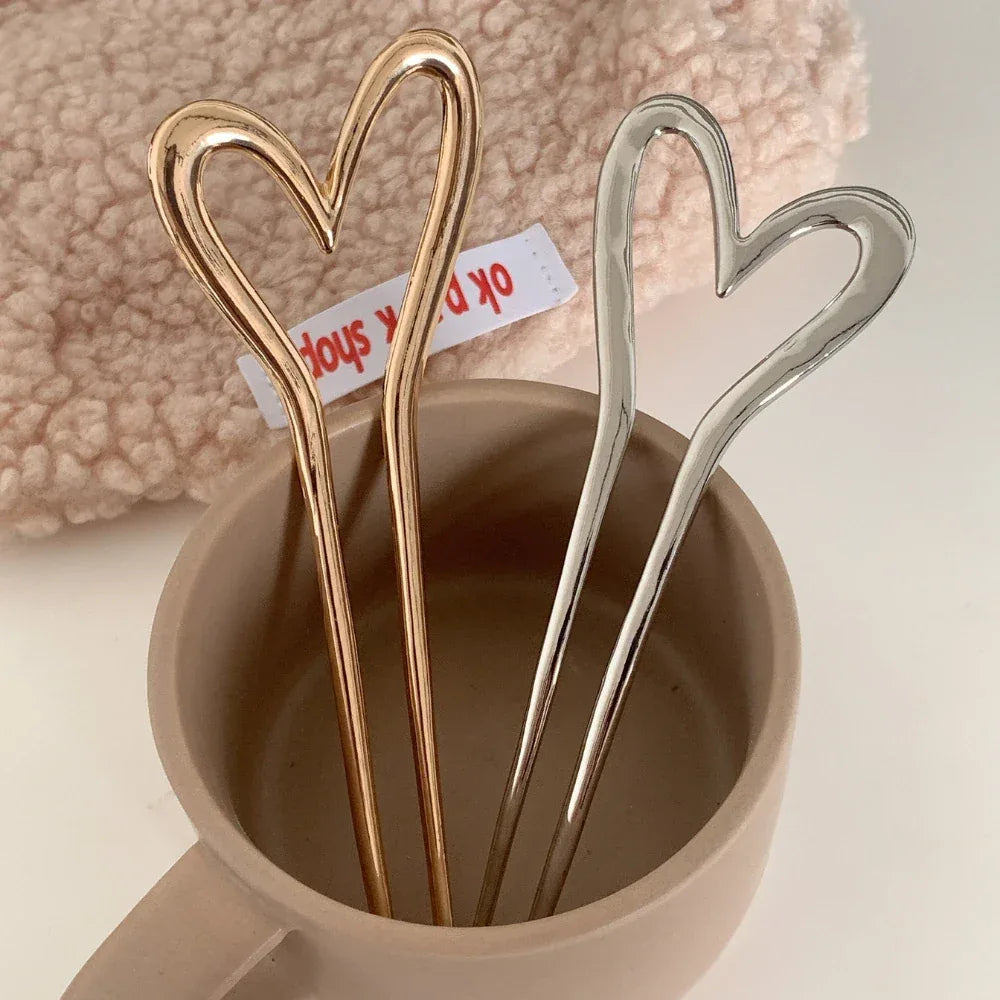 A gold-tone and a silver-tone heart-shaped hairpin standing upright in a light brown mug.