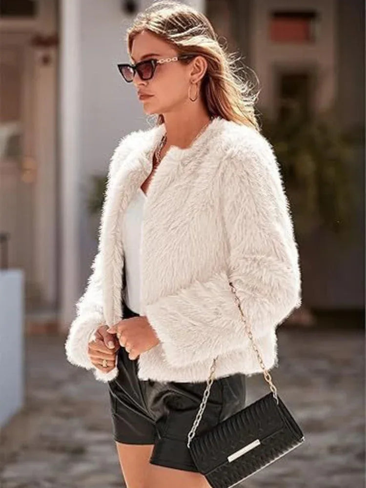 Woman wearing a white faux fur cropped jacket, white top, and black leather shorts, with a black handbag.