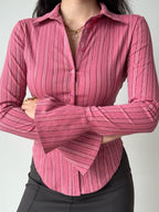 A woman with arms crossed, showcasing a pink striped long-sleeve shirt.