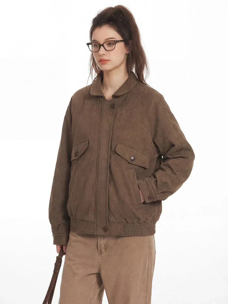 Close-up of a woman wearing a brown bomber jacket and tan pants, with one hand in her pocket.