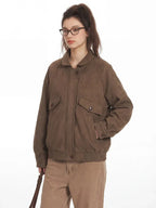 Close-up of a woman wearing a brown bomber jacket and tan pants, with one hand in her pocket.