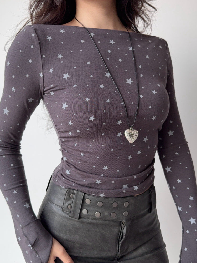 Model from the chest down wearing a grey long-sleeve top with a white star print and a heart-shaped locket.