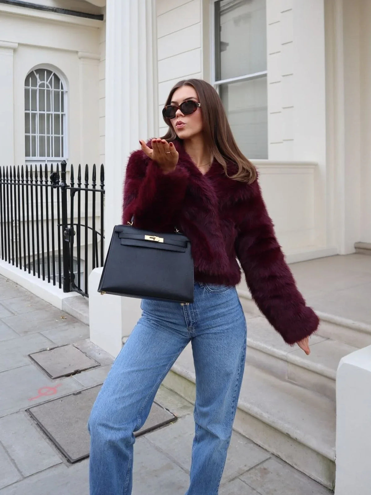 Woman wearing a burgundy faux fur jacket with blue jeans and a black handbag Main image