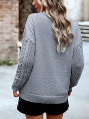 Back view of a woman wearing a grey knit sweater with cable knit sleeves and black shorts.