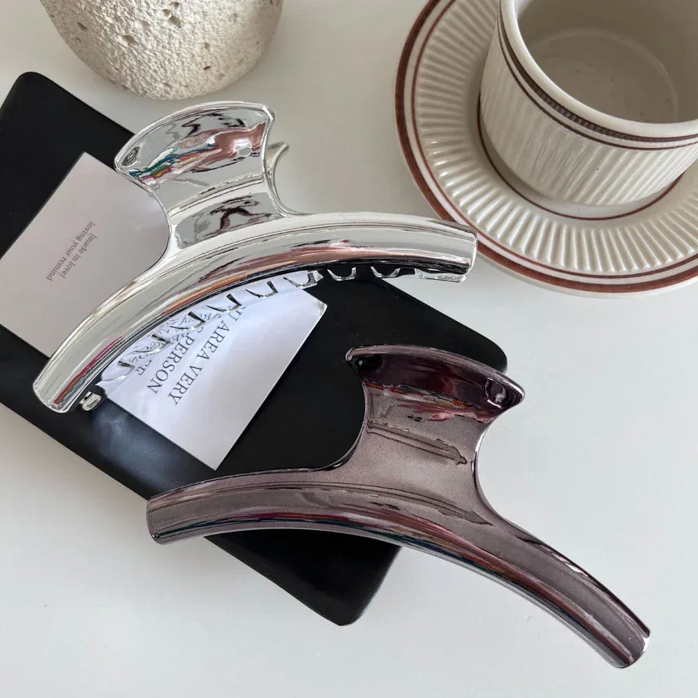Silver and dark grey metallic claw clips arranged on a black notebook and a white card