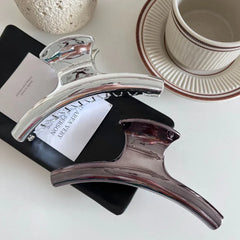 Silver and dark grey metallic claw clips arranged on a black notebook and a white card
