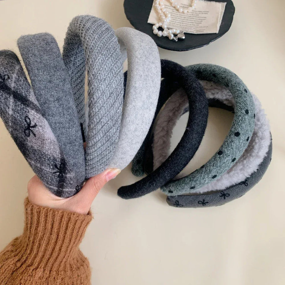 A hand holding a collection of padded headbands in various gray and green tones with different textures and patterns. Secondary image