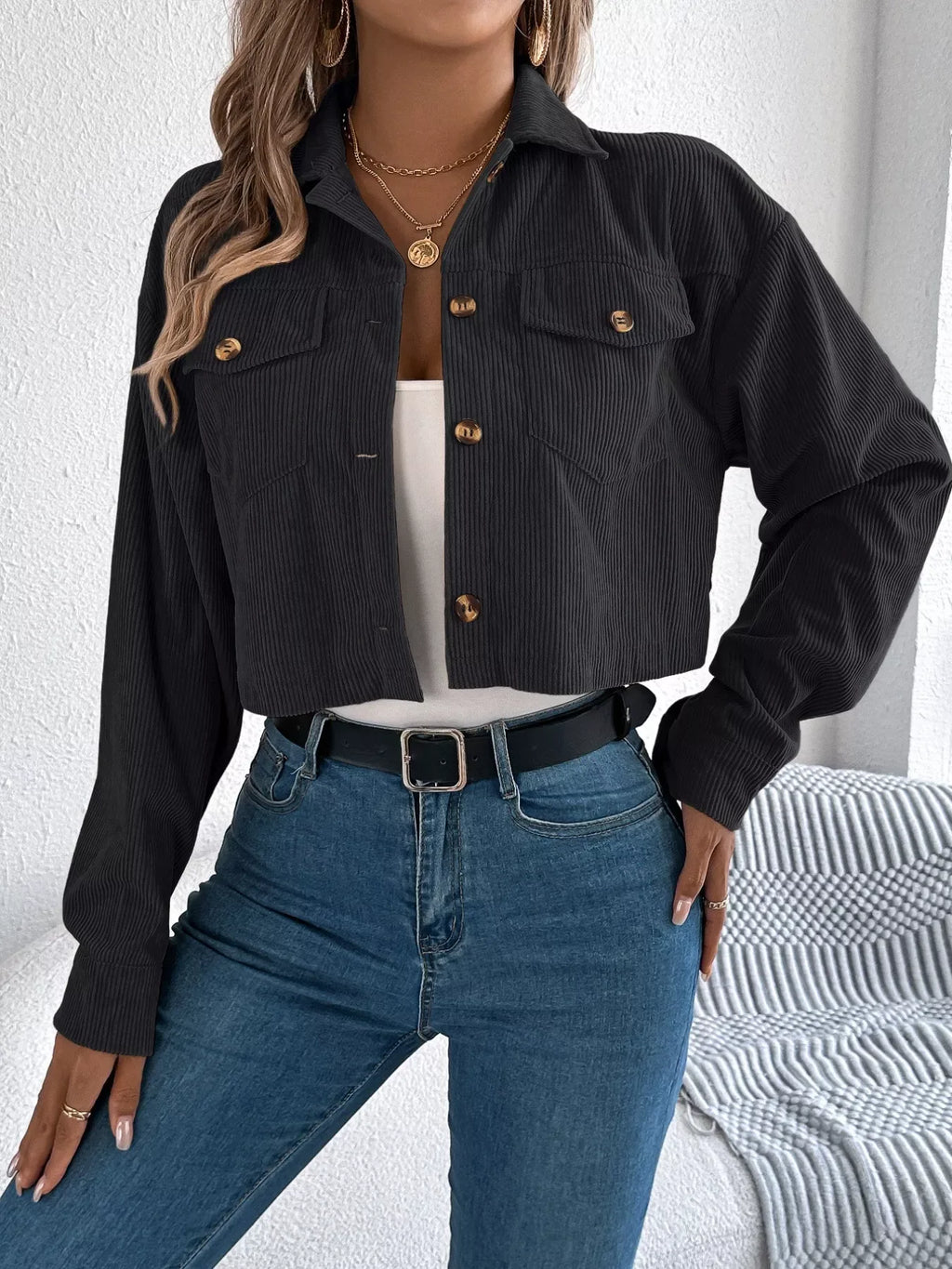Woman wearing a black corduroy cropped jacket over a white tank top and blue jeans, with her hand on her hip.