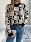 Woman wearing a black and white ghost print checkerboard knit sweater with blue jeans and a white clutch bag.