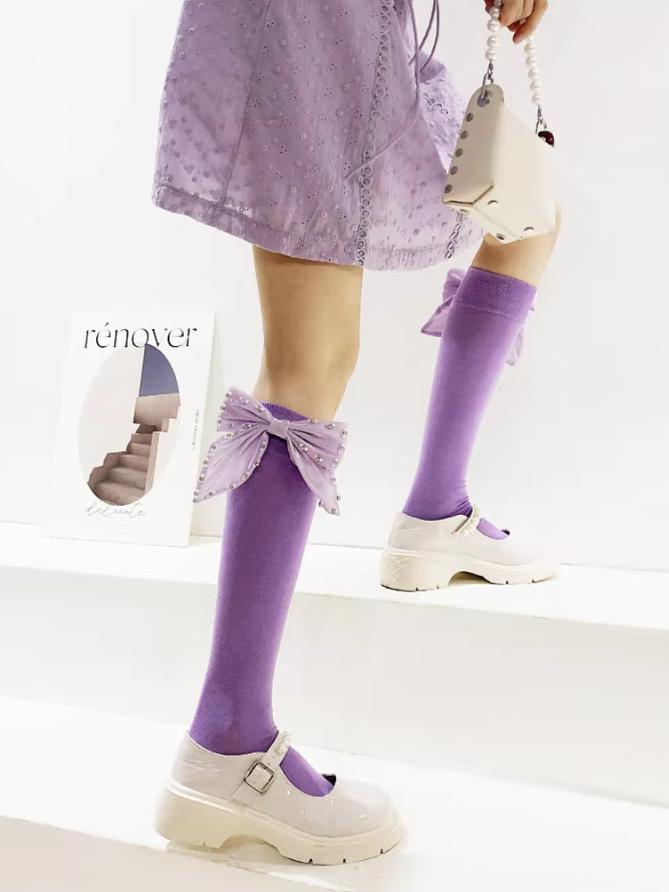A person climbing stairs wearing a purple dress, white Mary Jane shoes, and purple knee-high socks featuring large, embellished bows.