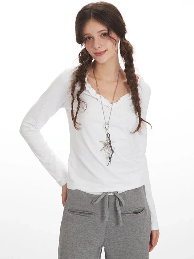Close-up of a woman wearing a white long-sleeve shirt with ruffled neckline and grey sweatpants, smiling and looking to the side.