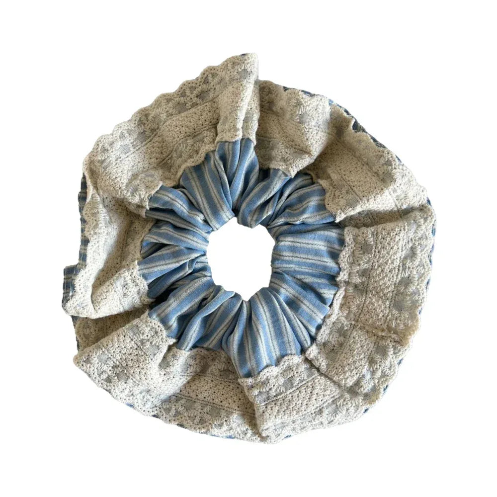 A close-up of a scrunchie with blue and white stripes and a lace trim.