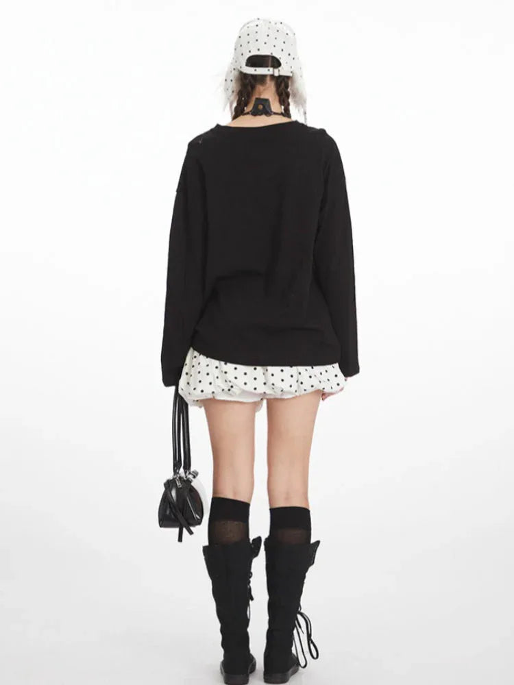 Back view of a young woman wearing a black long-sleeved graphic t-shirt, a white polka dot mini skirt, black knee-high socks, and black boots. She is carrying a black handbag.