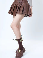 A person wearing brown pleated skirt, brown crew socks with a green creature applique, and brown loafers.