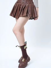 A person wearing brown pleated skirt, brown crew socks with a green creature applique, and brown loafers.