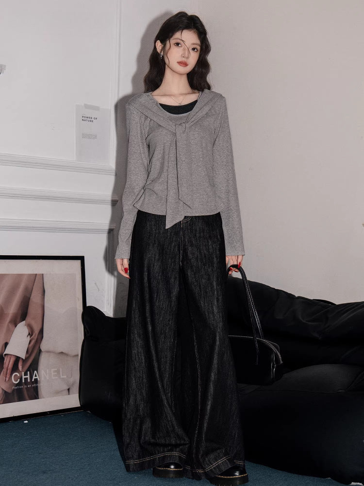 Full-body shot of a woman wearing a grey long-sleeved top with a draped overlay and wide-leg black jeans.