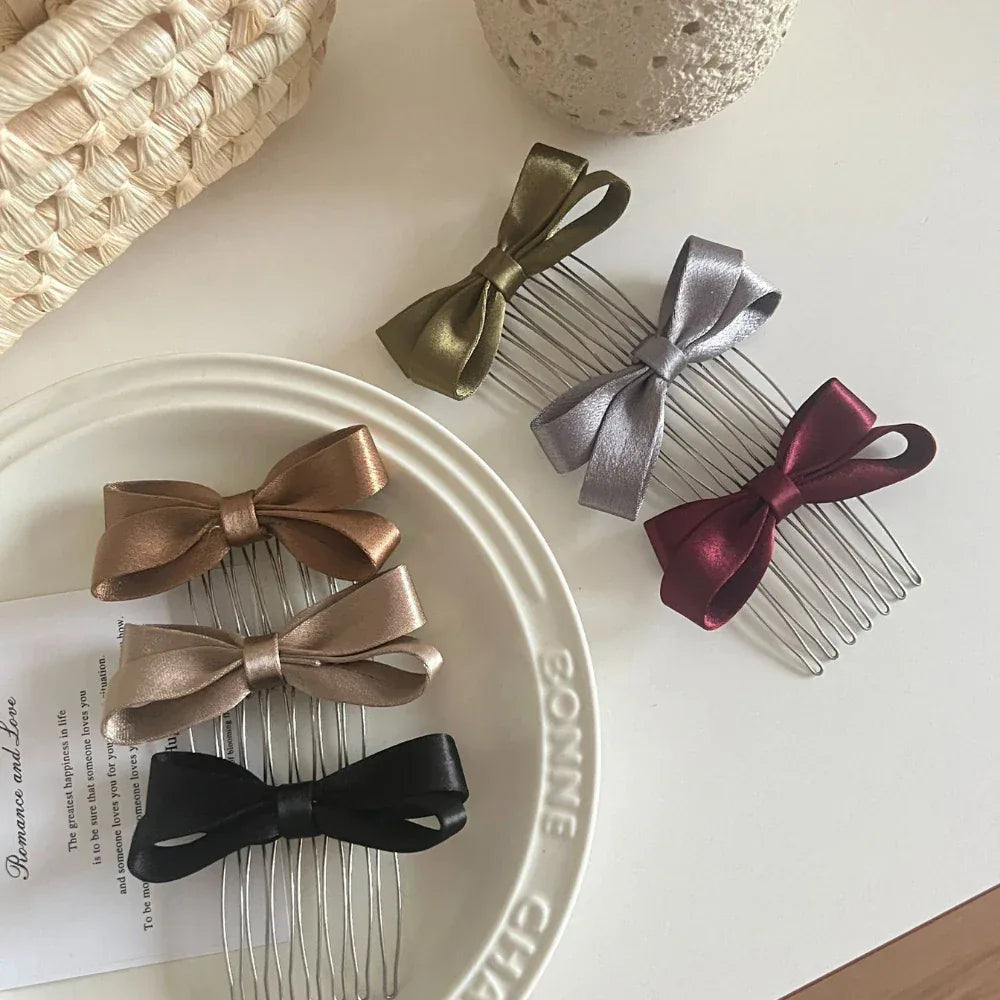 Several satin bow hair combs are arranged on a white plate and a white surface.
