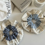 A top-down view of two scrunchies, one with light blue stripes and the other with dark blue stripes, both featuring delicate lace detailing.