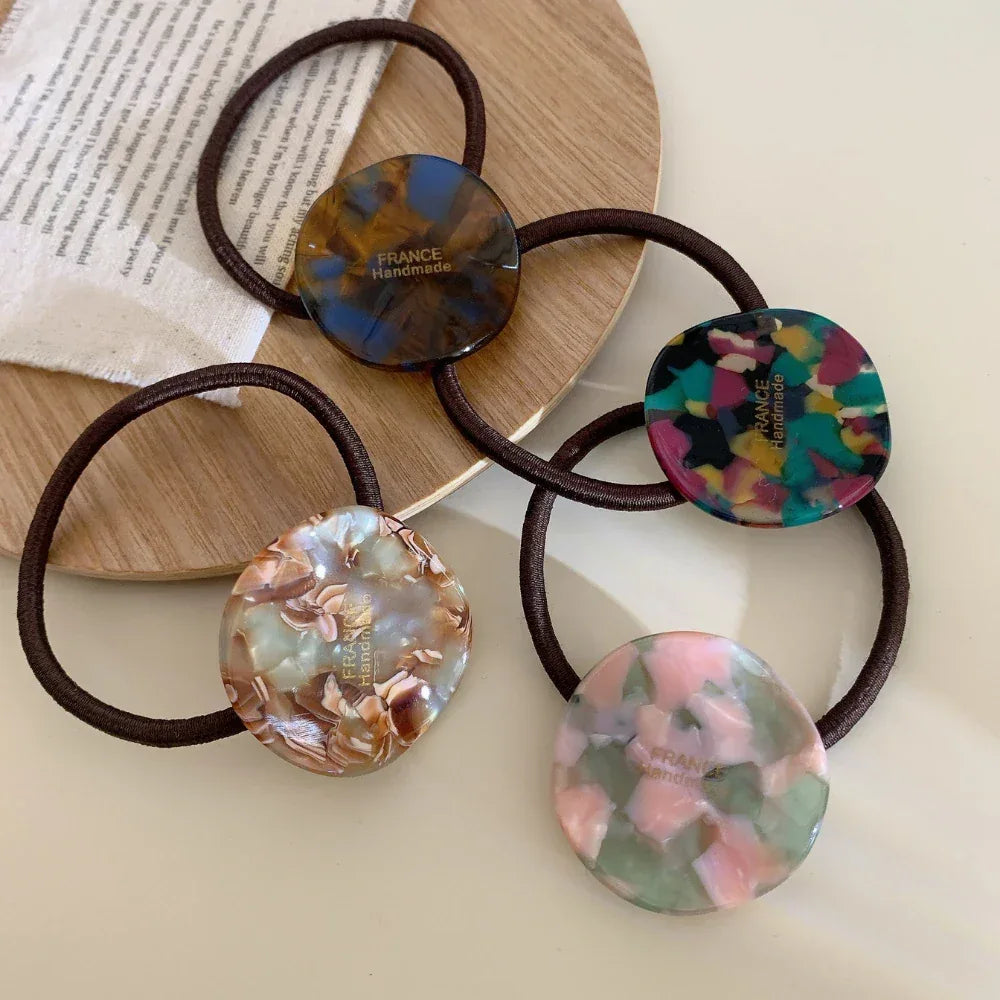 Four marbled round charm hair ties arranged on a wooden surface