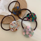 Four marbled round charm hair ties arranged on a wooden surface