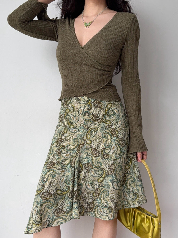 Woman wearing a green ribbed wrap top with a paisley print skirt and a yellow handbag