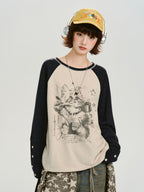 Front view of the model wearing the cream and navy raglan long-sleeve shirt with a cat graphic print and a yellow cap, showing the sleeve details.