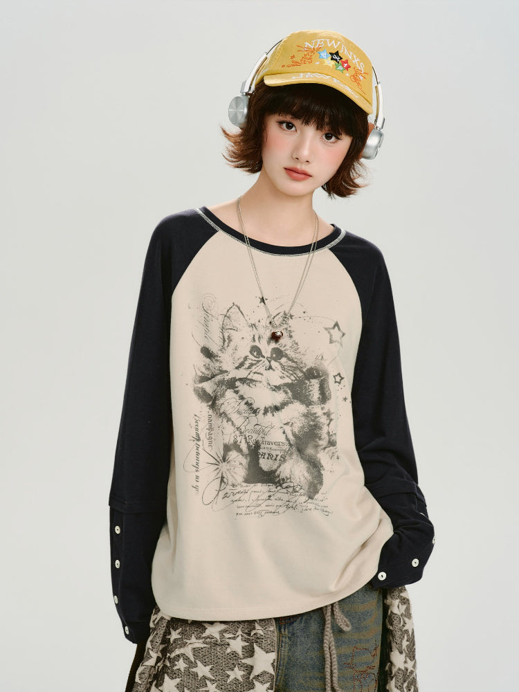 Front view of the model wearing the cream and navy raglan long-sleeve shirt with a cat graphic print and a yellow cap, showing the sleeve details.