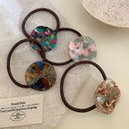 Five marbled round charm hair ties displayed on a beige cloth